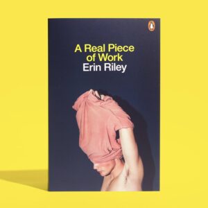 The front cover of the book 'A Real Piece of Work' by Erin Riley on a yellow background. The cover depicts someone taking off a pink t-shirt.